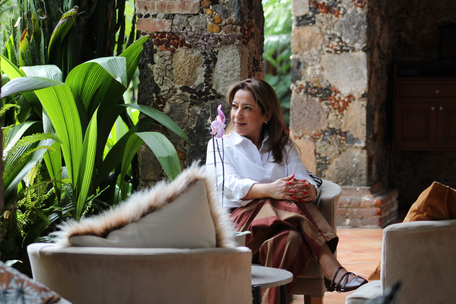 Xóchitl contempla el jardín sentada entre plantas y muros de piedra.